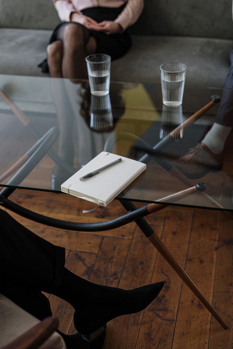 Szklany stół na którym stoją szklanki z wodą i notatnik z długopisem